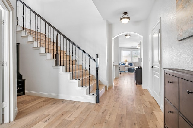 foyer with light wood-type flooring, arched walkways, baseboards, and stairway