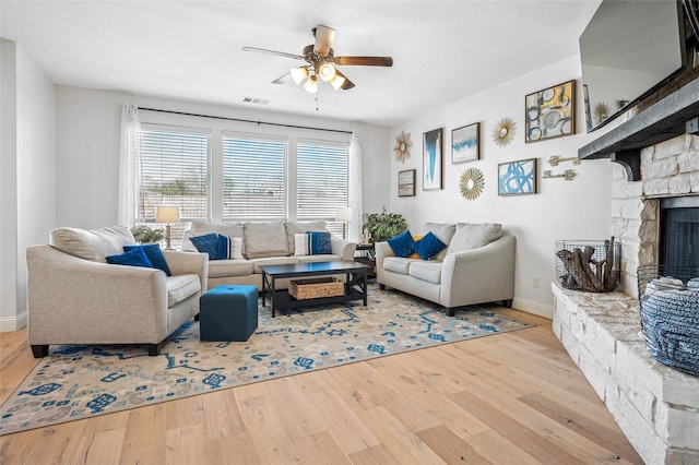 living room featuring a ceiling fan, baseboards, wood finished floors, visible vents, and a fireplace