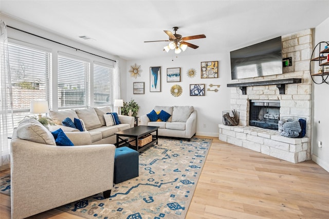 living room with visible vents, baseboards, ceiling fan, a fireplace, and wood finished floors