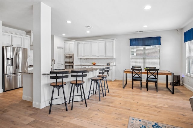 kitchen featuring backsplash, light wood-type flooring, a kitchen breakfast bar, white cabinets, and stainless steel appliances