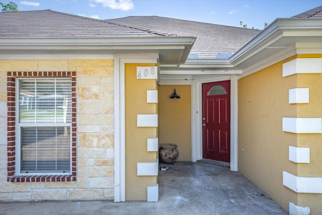 doorway to property featuring stone siding and a shingled roof