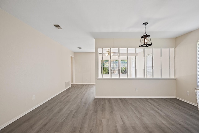 unfurnished room with a ceiling fan, visible vents, wood finished floors, and baseboards