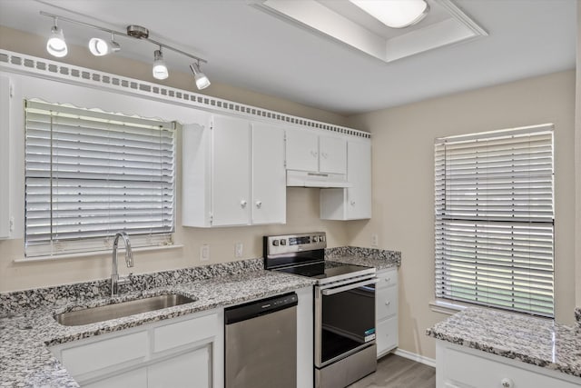 kitchen featuring light stone countertops, a sink, stainless steel appliances, under cabinet range hood, and white cabinetry