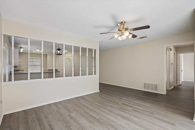 spare room with wood finished floors, a ceiling fan, visible vents, and baseboards