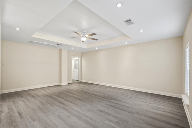 empty room with a tray ceiling, wood finished floors, a ceiling fan, and visible vents