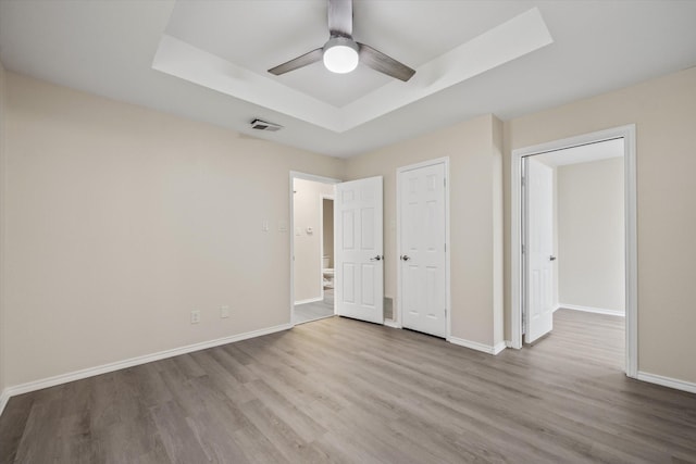 unfurnished bedroom with visible vents, a raised ceiling, baseboards, and wood finished floors