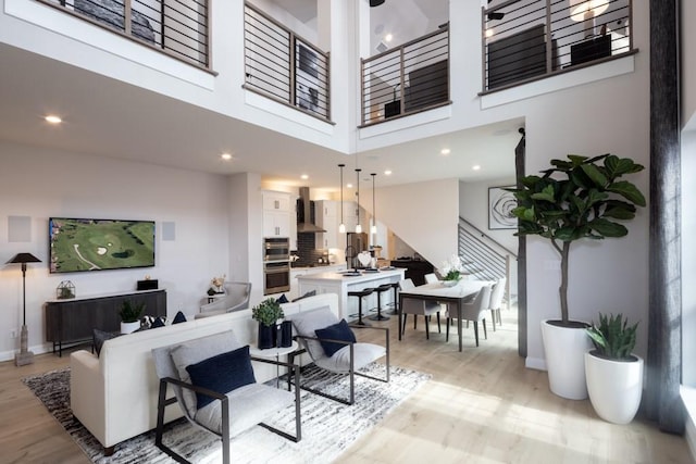 living area with recessed lighting, light wood-style flooring, baseboards, and a towering ceiling