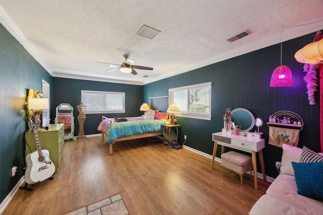 bedroom featuring visible vents, ornamental molding, wood finished floors, a textured ceiling, and a ceiling fan