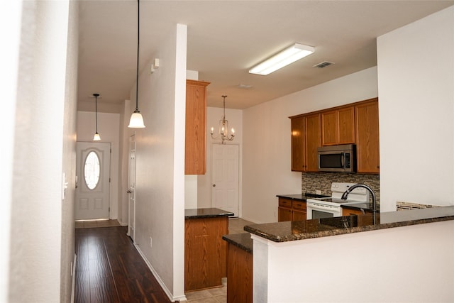 kitchen featuring tasteful backsplash, stainless steel microwave, dark stone countertops, electric stove, and brown cabinetry