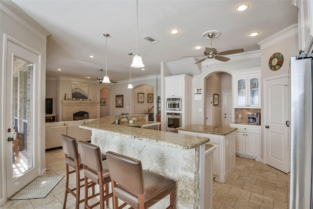 kitchen featuring arched walkways, visible vents, an island with sink, and ceiling fan