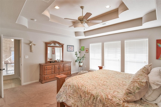 bedroom with visible vents, baseboards, light colored carpet, a tray ceiling, and multiple windows