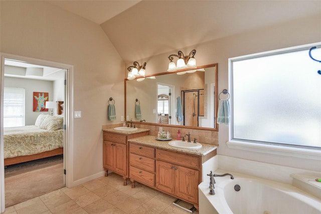 ensuite bathroom with plenty of natural light, lofted ceiling, and a sink