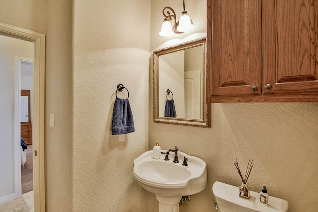 half bathroom featuring a sink, toilet, tile patterned floors, and a textured wall