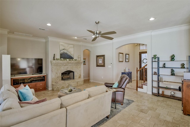 living area with visible vents, ceiling fan, ornamental molding, a fireplace, and arched walkways