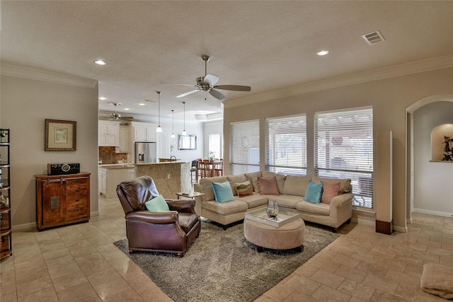 living area featuring crown molding, baseboards, visible vents, and ceiling fan