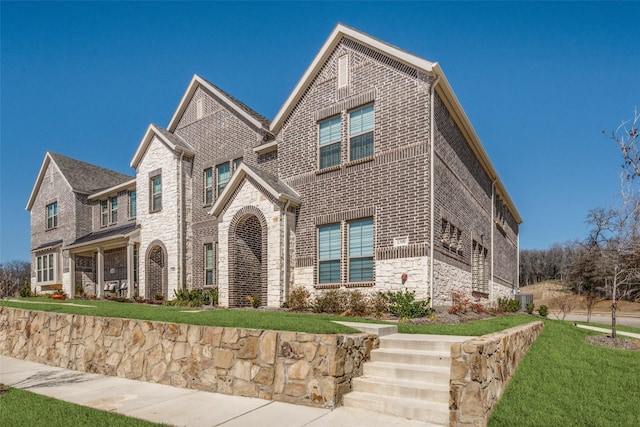 view of front of house featuring brick siding, stone siding, and a front lawn