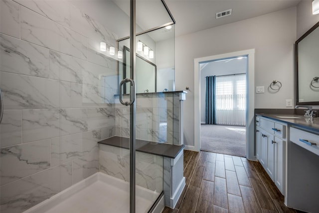 bathroom featuring visible vents, wood tiled floor, a shower stall, baseboards, and vanity