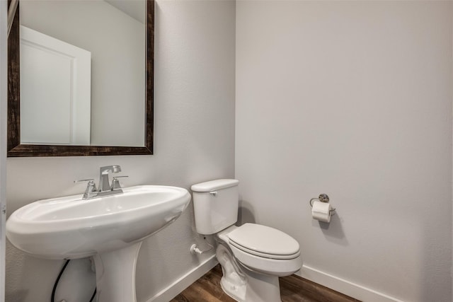 half bath featuring a sink, toilet, baseboards, and wood finished floors