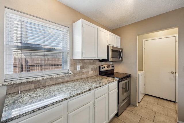 kitchen with backsplash, washer / dryer, appliances with stainless steel finishes, light tile patterned flooring, and white cabinetry