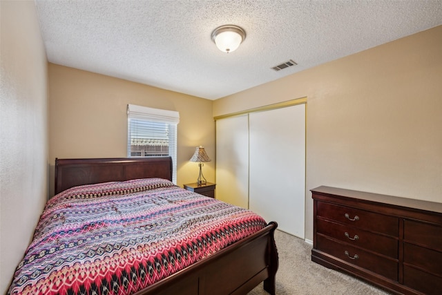 carpeted bedroom with visible vents, a textured ceiling, and a closet