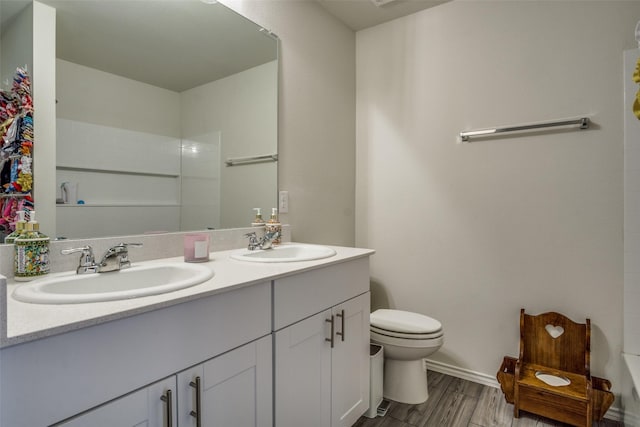 bathroom with double vanity, toilet, wood finished floors, and a sink