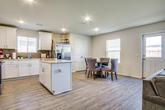 kitchen featuring backsplash, a center island, stainless steel fridge with ice dispenser, light countertops, and light wood-style flooring