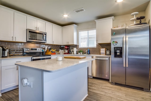 kitchen featuring a kitchen island, light wood-style flooring, stainless steel appliances, decorative backsplash, and white cabinets