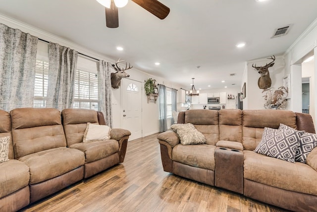 living room featuring visible vents, crown molding, recessed lighting, ceiling fan with notable chandelier, and light wood-style floors