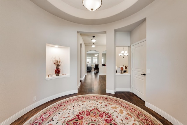 foyer with an inviting chandelier, dark wood-type flooring, baseboards, and arched walkways