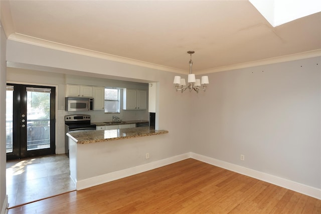 kitchen featuring baseboards, light wood finished floors, a peninsula, appliances with stainless steel finishes, and a notable chandelier