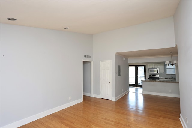 unfurnished living room with light wood finished floors, visible vents, an inviting chandelier, and baseboards