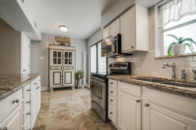 kitchen with stone counters, backsplash, white cabinets, appliances with stainless steel finishes, and a sink