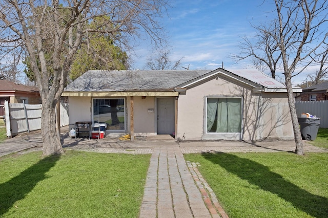 back of house featuring fence, a lawn, and stucco siding