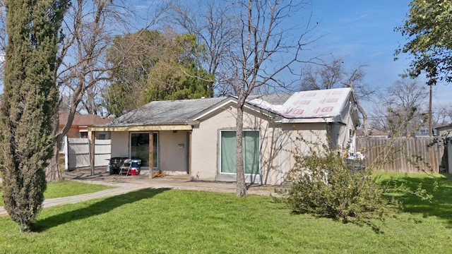 back of house featuring stucco siding, a lawn, and fence