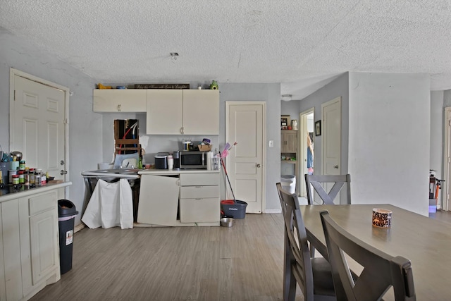 kitchen with stainless steel microwave, light wood-style flooring, light countertops, and a textured ceiling