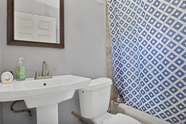 full bath featuring a sink, curtained shower, toilet, and a textured wall