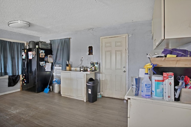 kitchen with black fridge, a textured ceiling, wood finished floors, white cabinetry, and light countertops