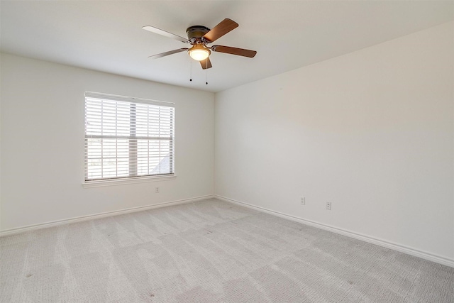 empty room featuring a ceiling fan, light colored carpet, and baseboards