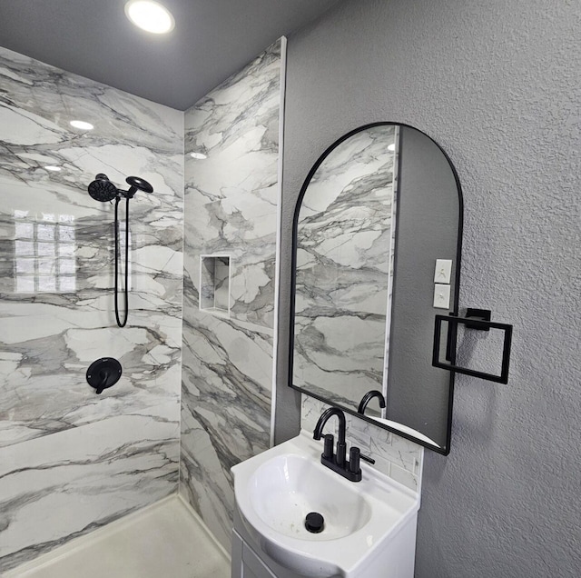 bathroom with a textured wall, a marble finish shower, and a sink