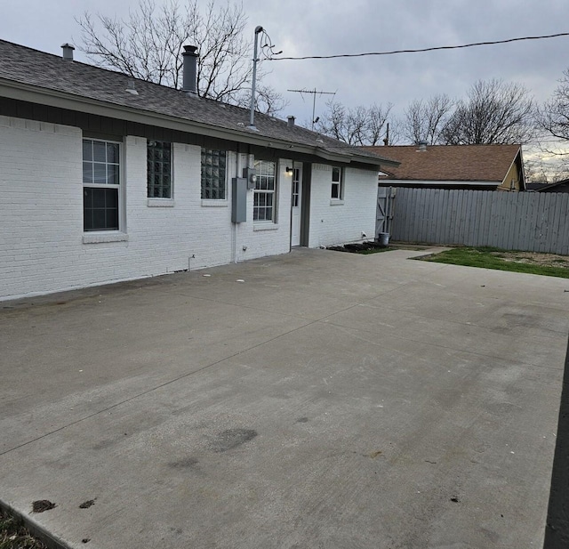 rear view of house with brick siding, roof with shingles, a patio, and fence