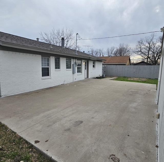 rear view of property with a patio area, fence, brick siding, and a shingled roof