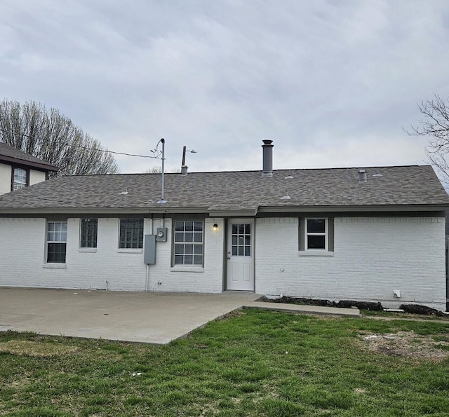 back of property with brick siding, a patio area, a lawn, and a shingled roof