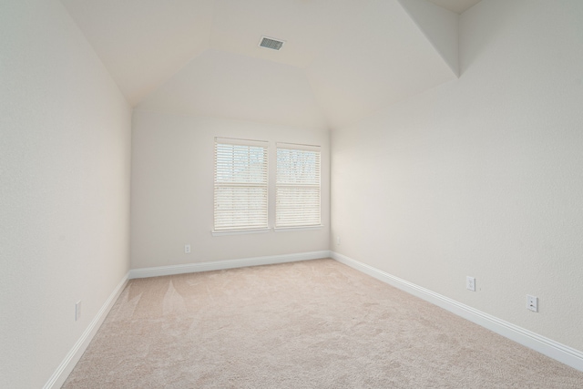 unfurnished room featuring light carpet, visible vents, baseboards, and vaulted ceiling