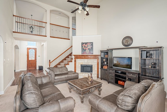 living area with a ceiling fan, arched walkways, a stone fireplace, baseboards, and a towering ceiling