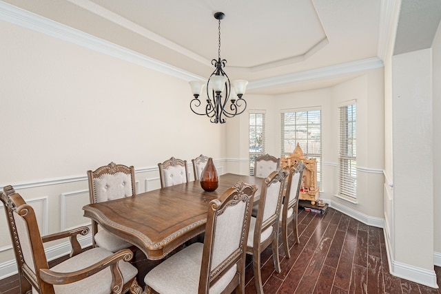 dining area with dark wood finished floors, a chandelier, a tray ceiling, wainscoting, and a decorative wall