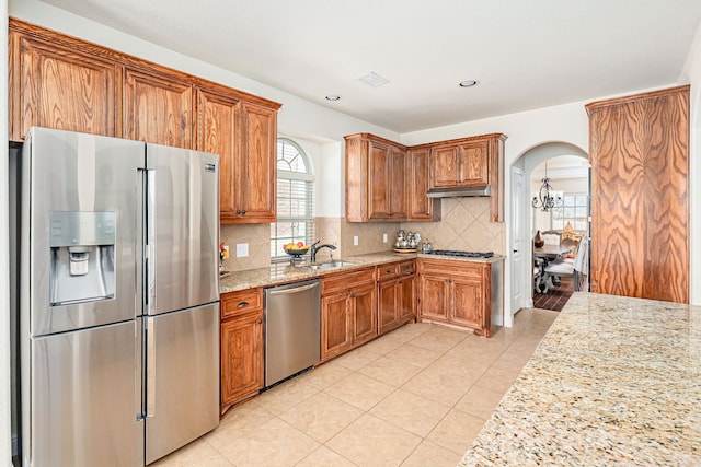 kitchen with light stone countertops, under cabinet range hood, decorative backsplash, appliances with stainless steel finishes, and a sink