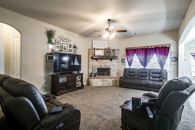 carpeted living room featuring visible vents, baseboards, ceiling fan, a fireplace, and arched walkways