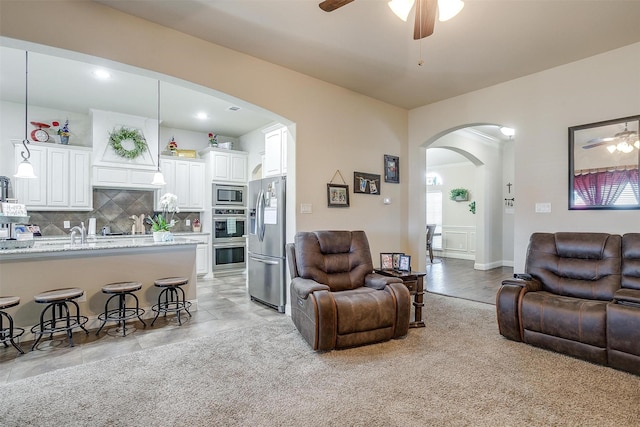 living area with a ceiling fan, arched walkways, and light carpet