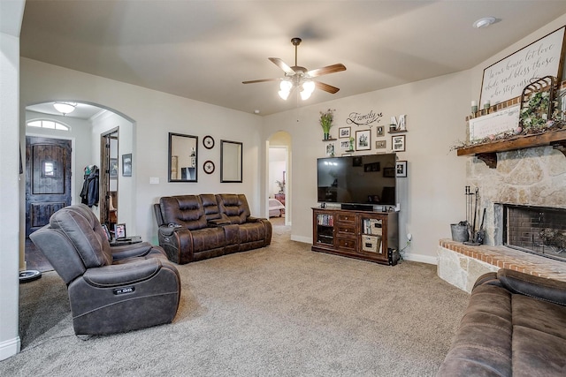 carpeted living area with baseboards, arched walkways, a stone fireplace, and ceiling fan