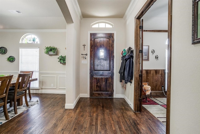 entrance foyer with visible vents, crown molding, dark wood-type flooring, a wainscoted wall, and arched walkways